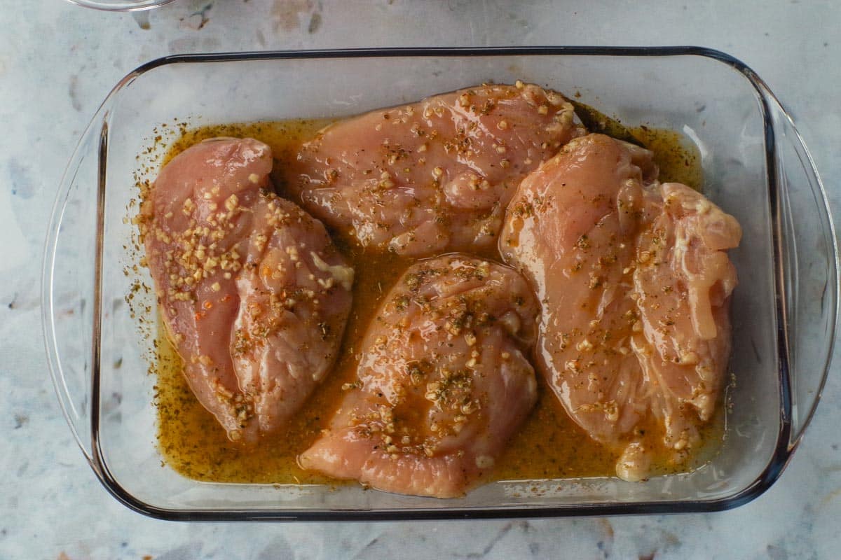 Marinade poured over chicken in glass container.