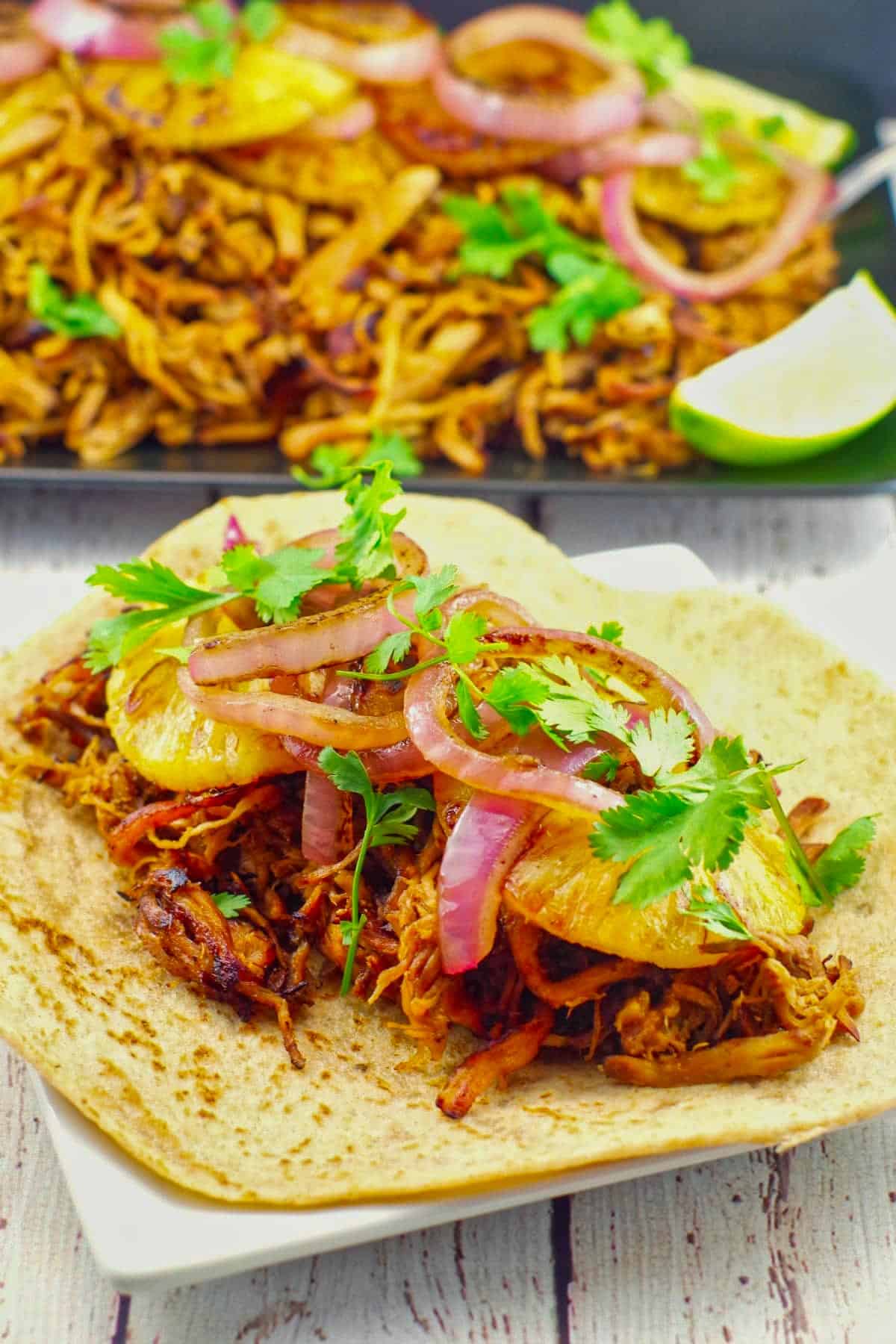 Pineapple Pork Carnita on a white plate with a platter of more carnita meat in the background.