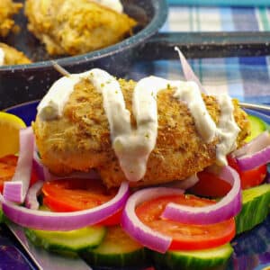 Weight Watchers Greek Chicken Souvlaki on a bed of vegetables, with some tzatziki drizzled over it.