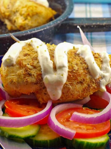 Weight Watchers Greek Chicken Souvlaki on a bed of vegetables, with some tzatziki drizzled over it.