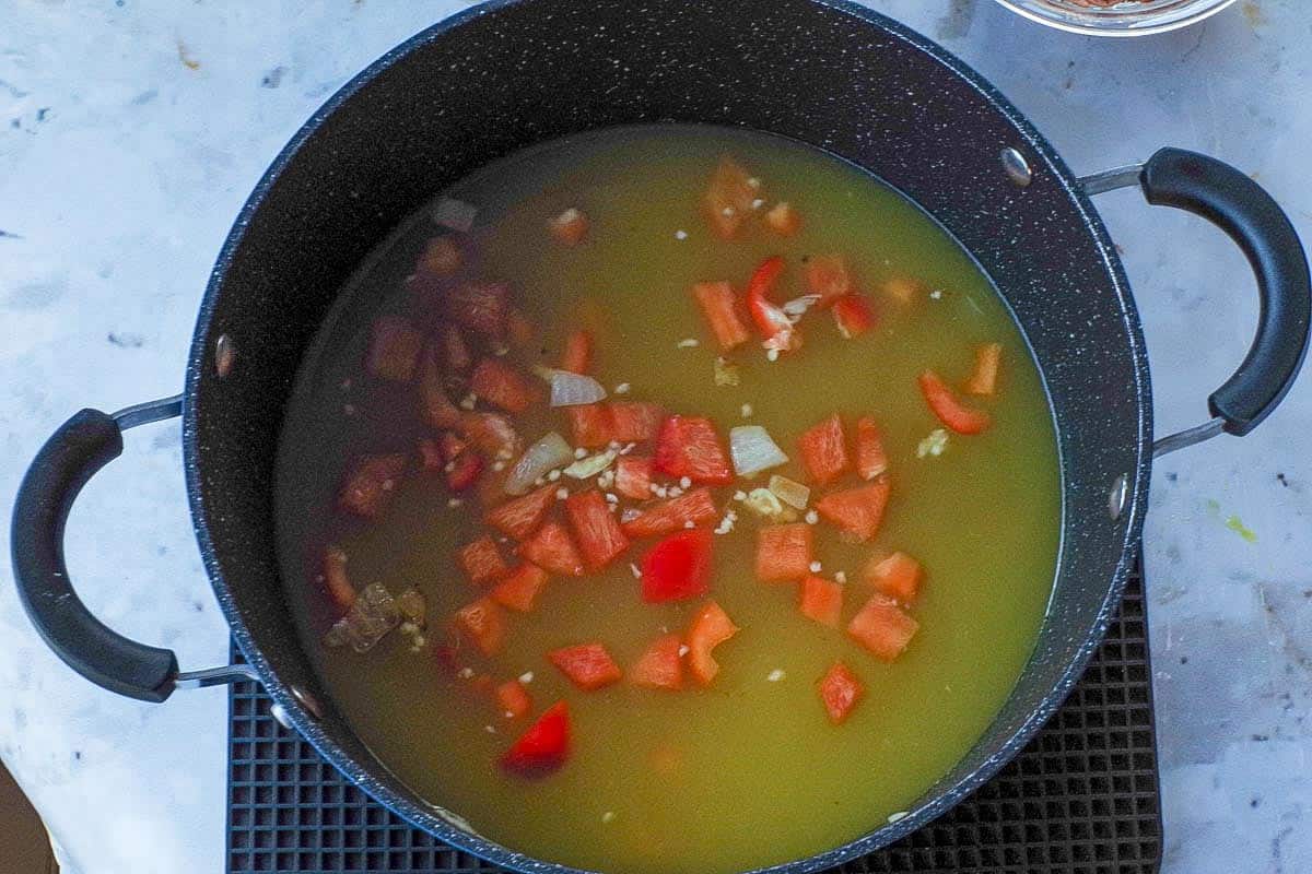 Pot with chicken broth, garlic and red pepper added to the onions.