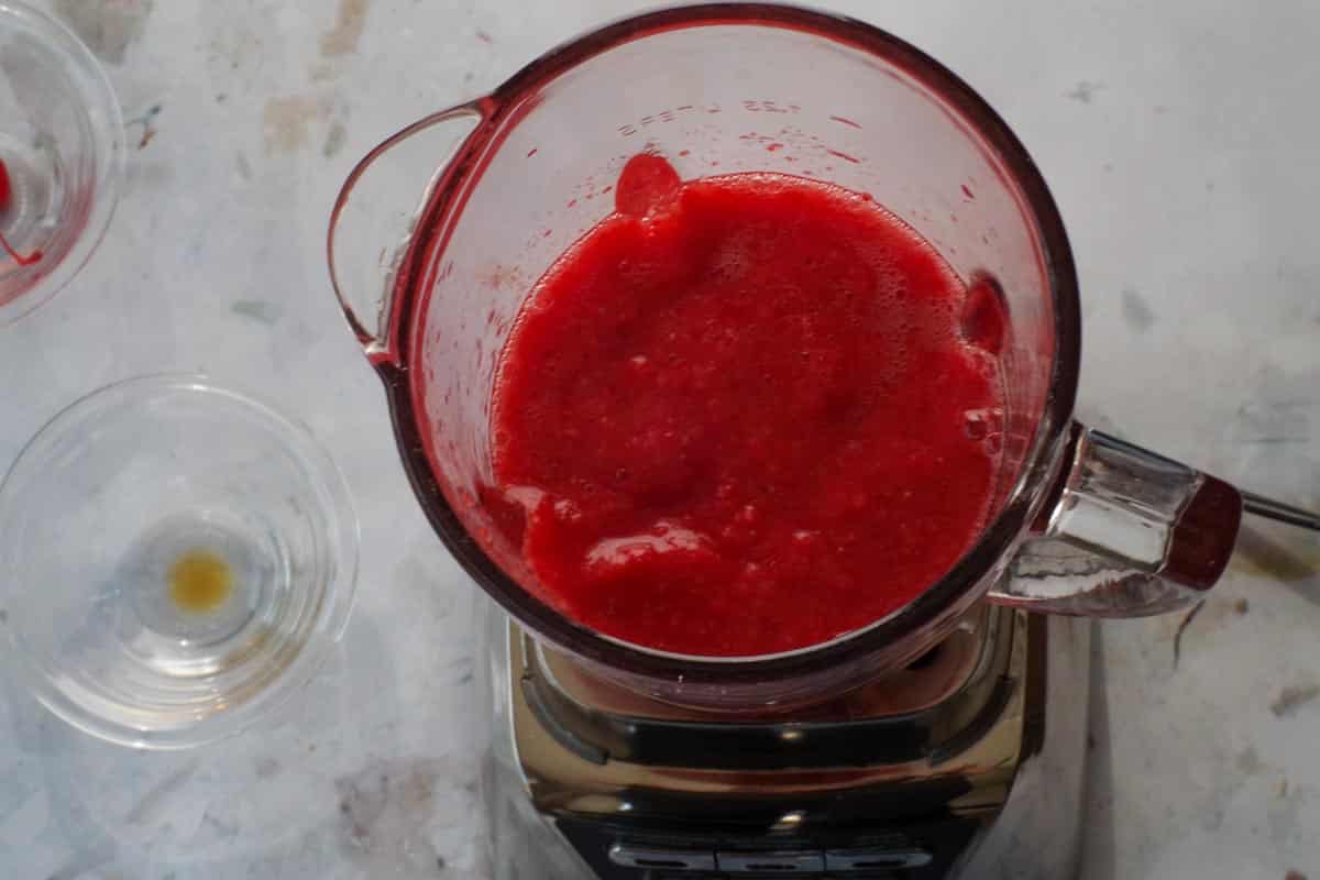 Frozen strawberries and Daiquiri mix blended together in bowl of a blender.