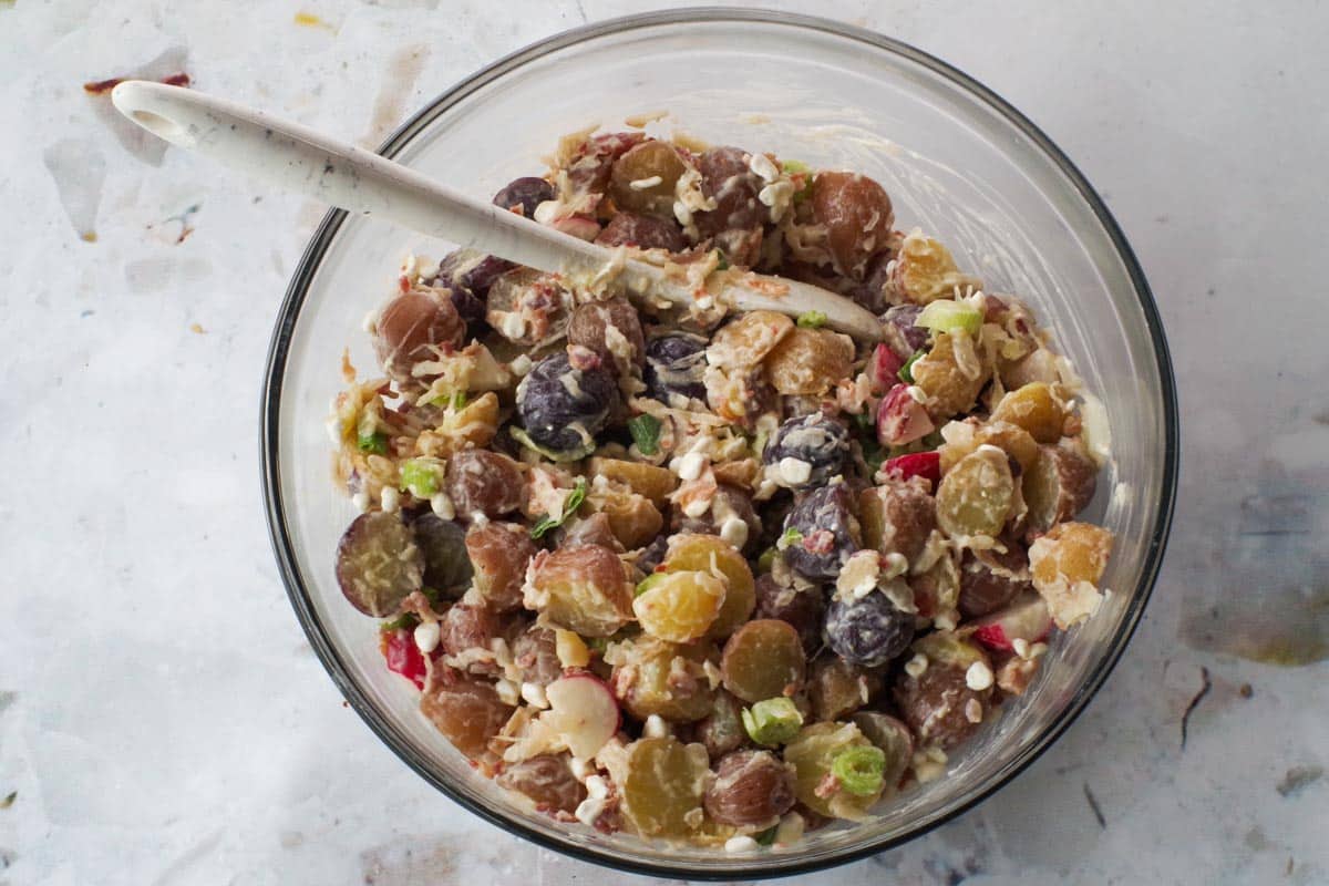 Potato salad mixed together in large glass bowl with marble silicone spoon.