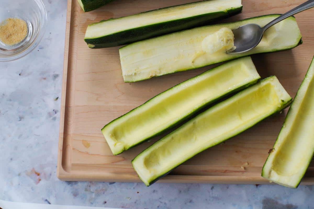 Using a spoon to hollow out zucchini halves.