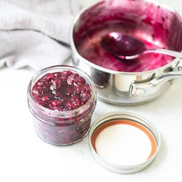 Saskatoon Berry Jam in a jar with an empty pot (where it was cooked) beside it.