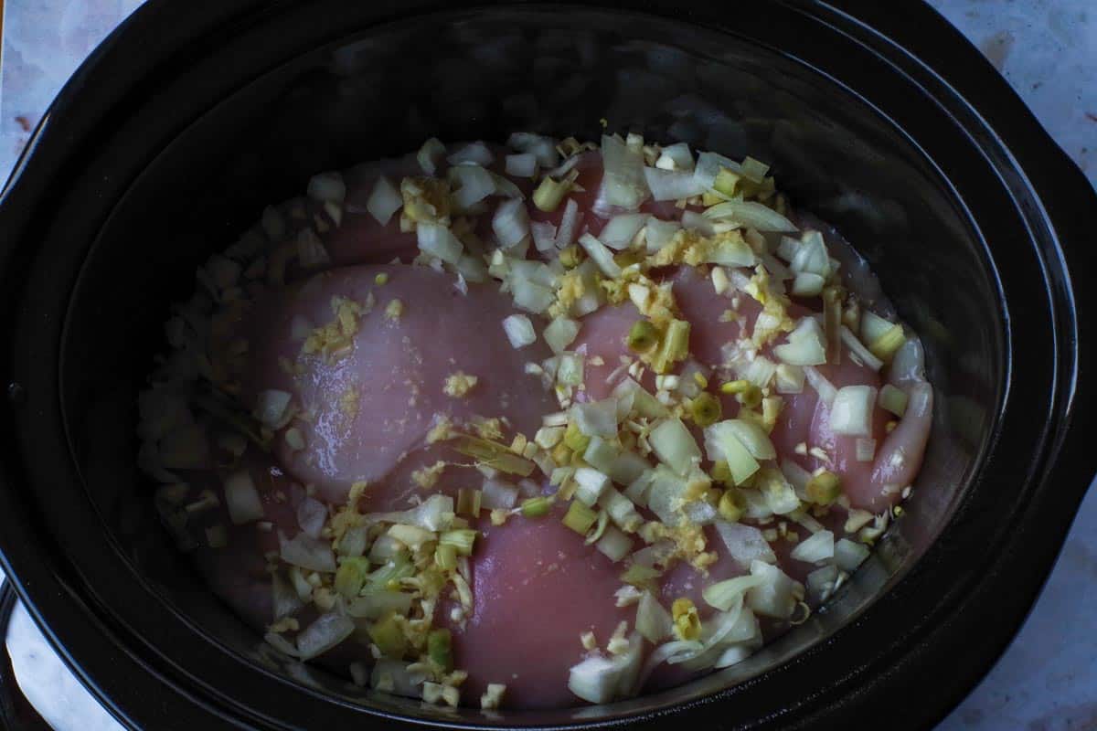 Chicken breast in slow cooker with onion, garlic, ginger, and lemon grass.