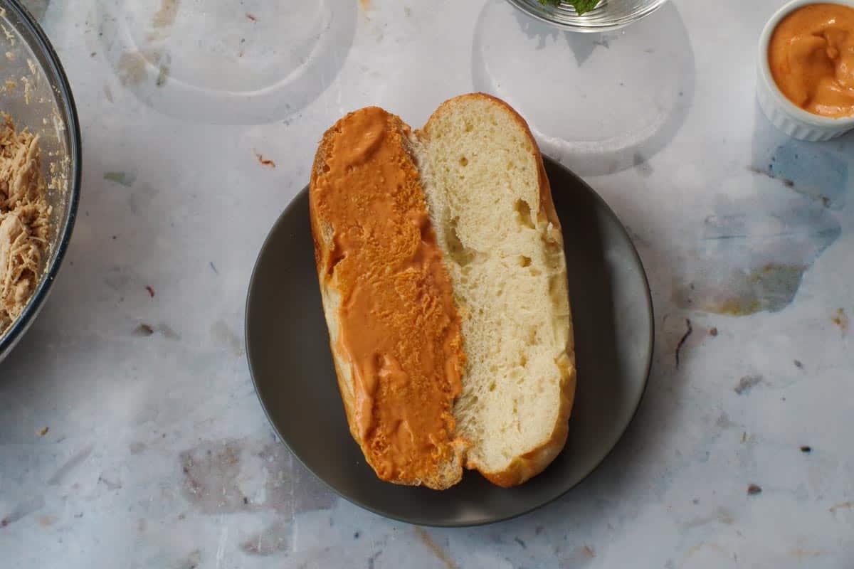 Sriracha mayo spread on one side of the bun on a black plate.