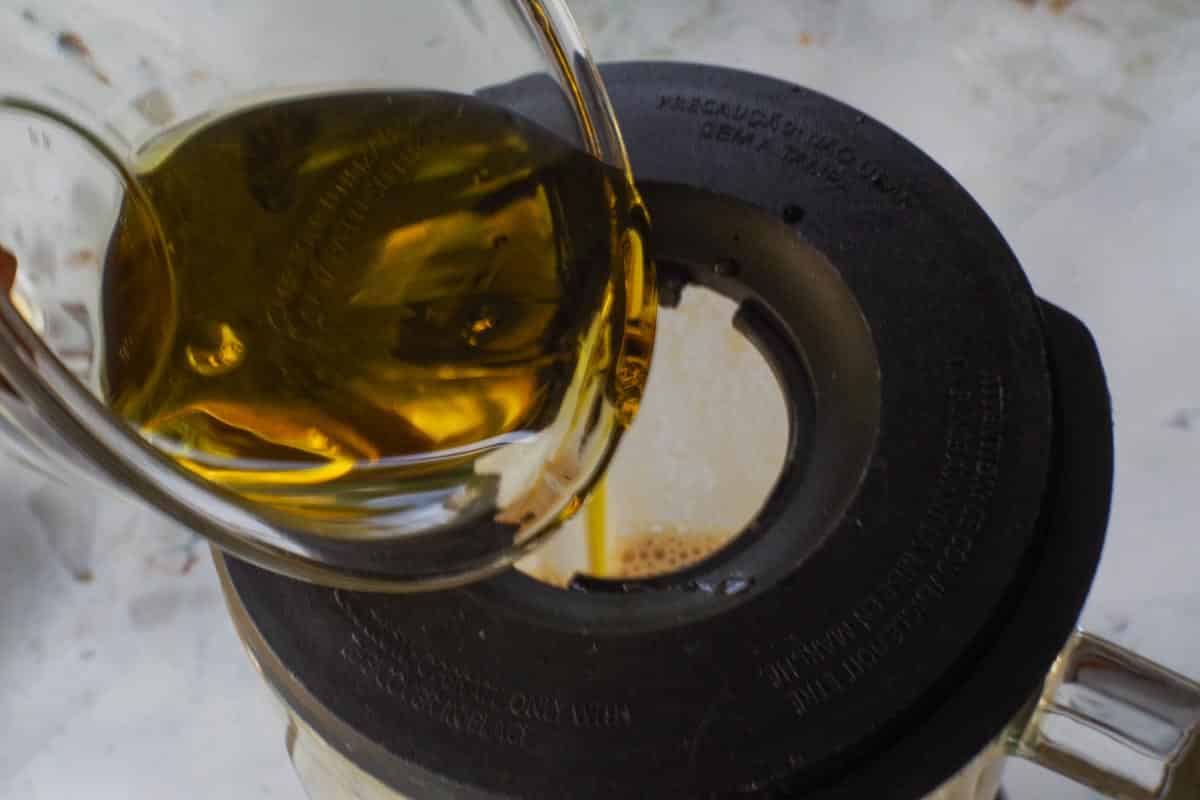 Olive oil being poured through the hole in the lid of the blender.