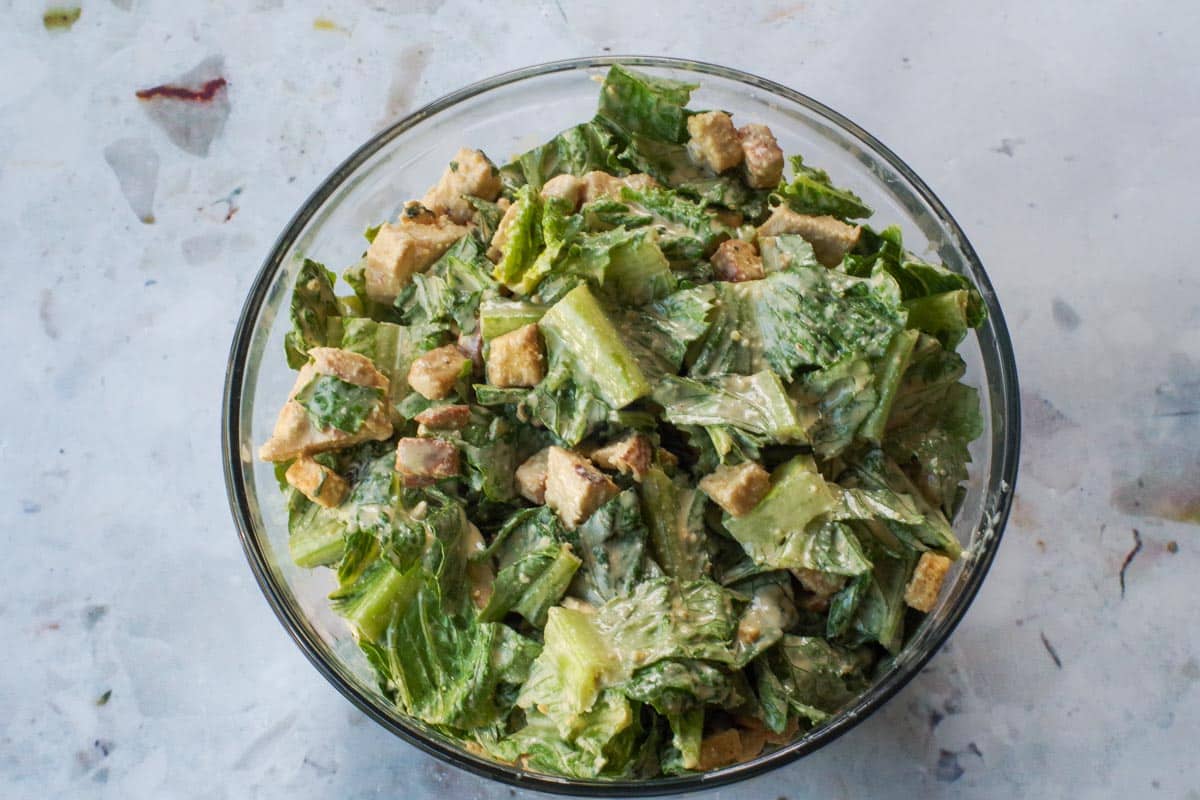 All ingredients in Grilled Chicken Caesar salad mixed together in a large glass bowl.