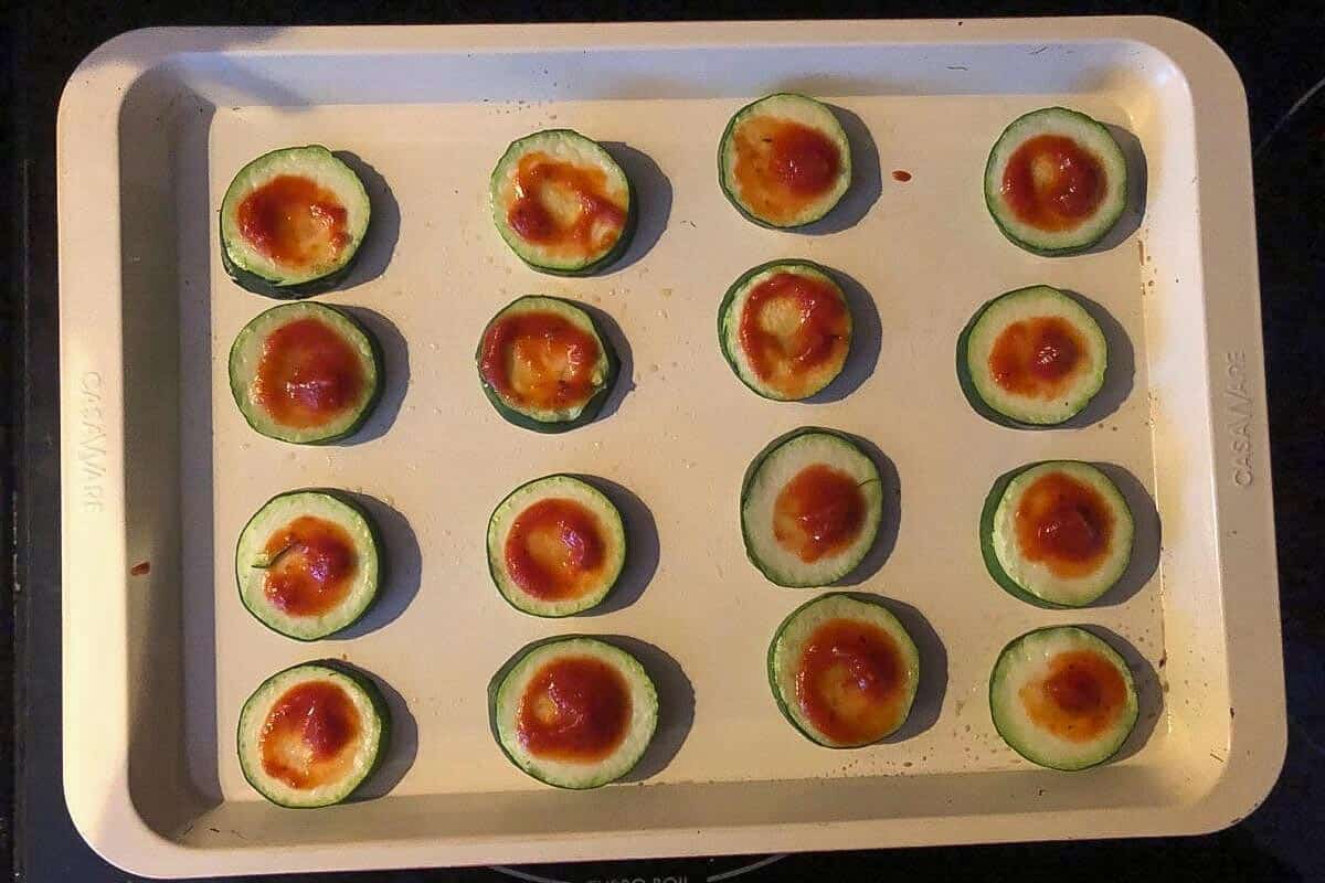 Zucchini bites with pizza sauce on a baking sheet.