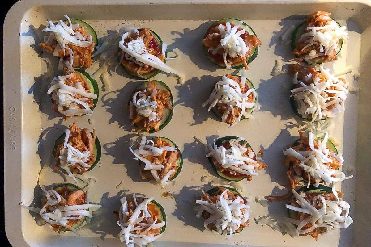 Cheese sprinkled over chicken and pizza sauce on zucchini bites.