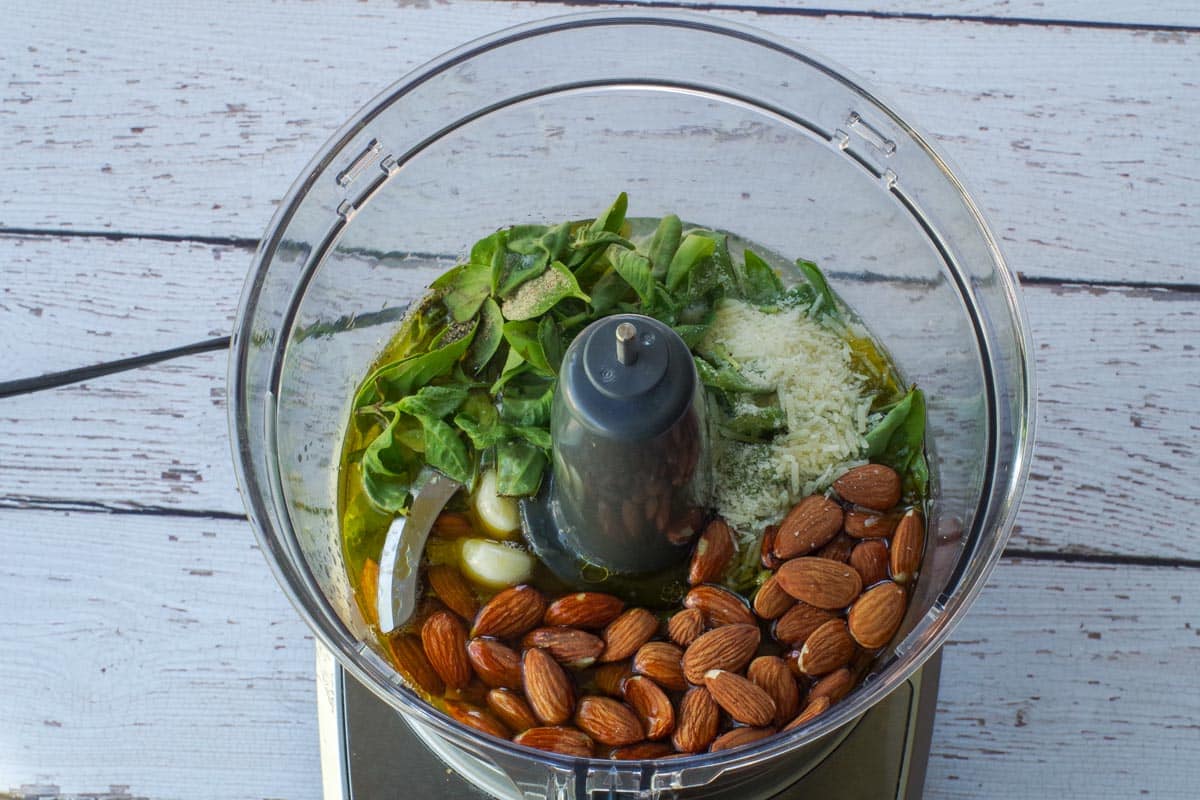 All ingredients for almond basil pesto in the bowl of a food processor.