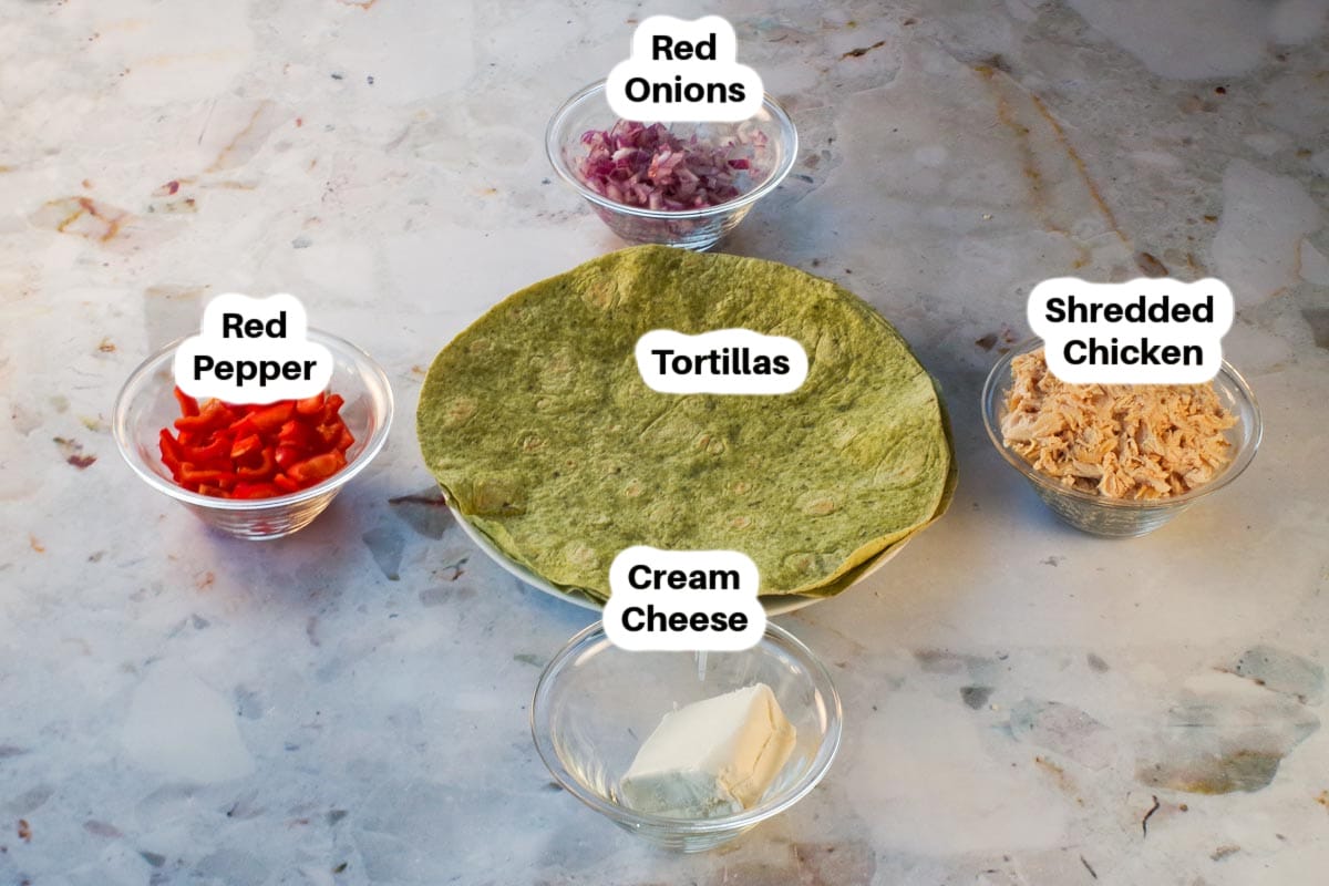 ingredients needed for chicken pinwheels in glass bowls, labelled, with tortillas in the middle.
