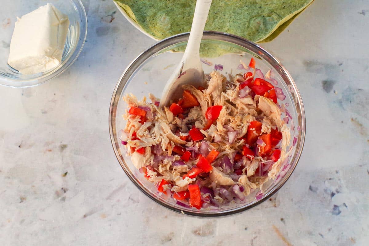 Chicken, red onion and red pepper mixed together in glass bowl with silicone spoon.