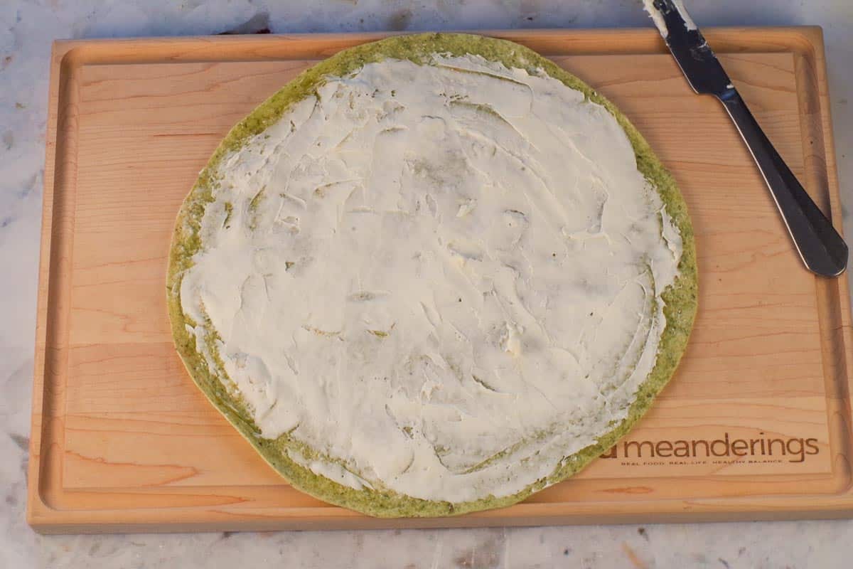 cream cheese spread onto tortilla on cutting board.