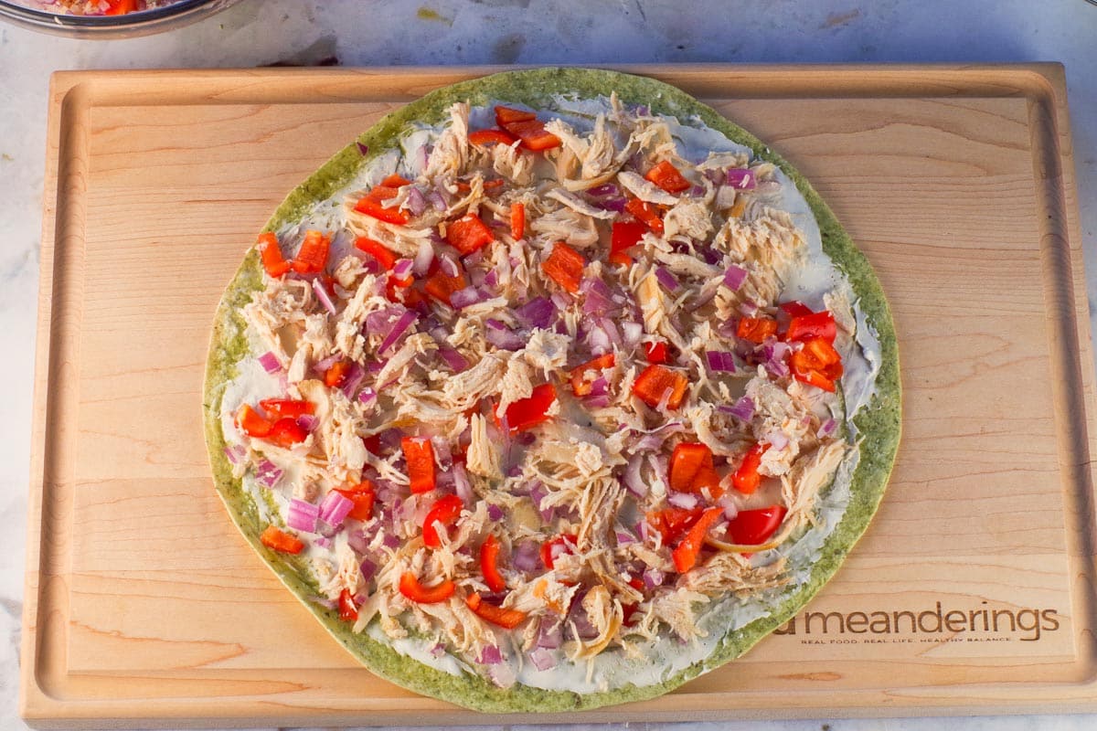 Chicken mixture spread on tortilla on wooden cutting board.