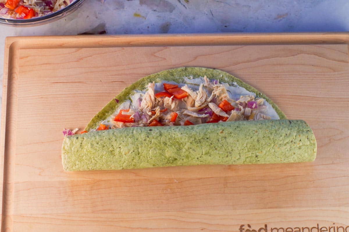 Chicken Tortilla being rolled up to near the top on wooden cutting board.