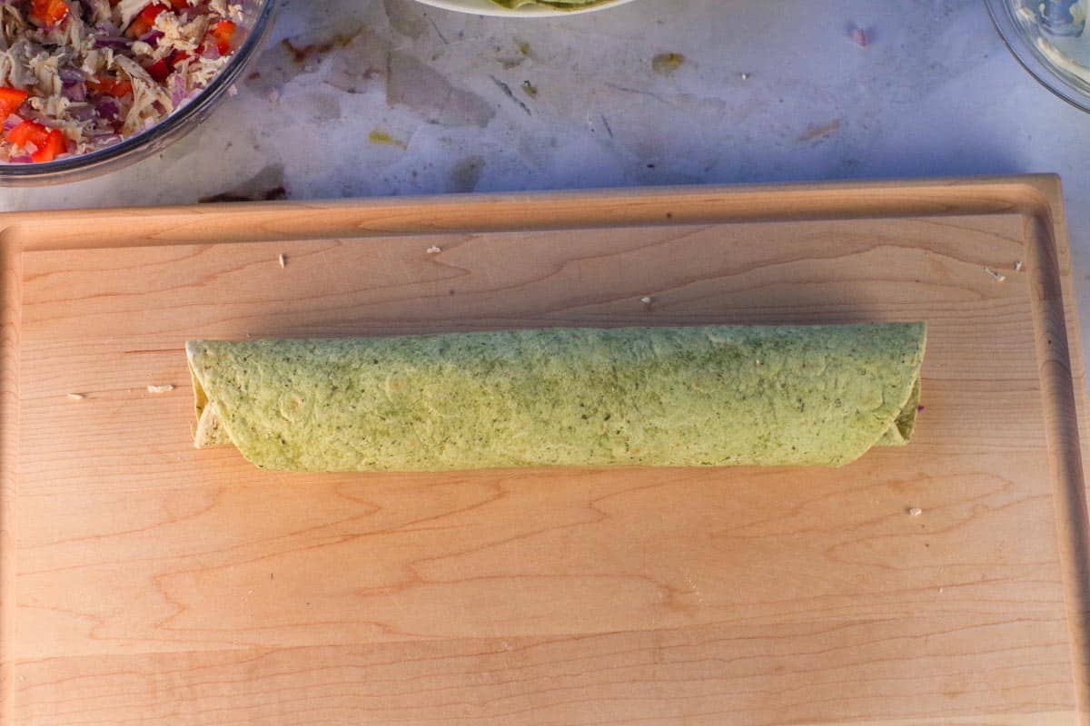 Chicken tortilla rolled right up to the end, on cutting board, seam side down.