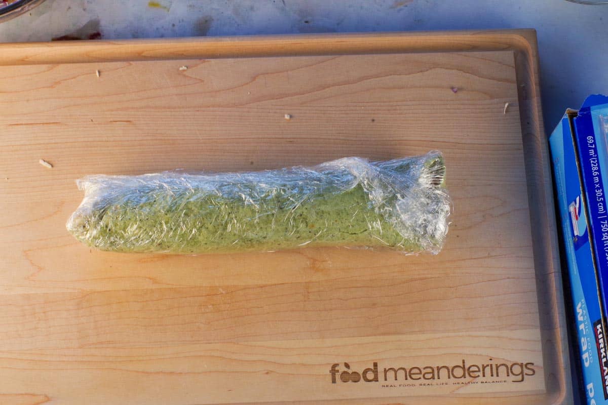 Fille and rolled tortilla wrapped in plastic wrap, on a wooden cutting board.