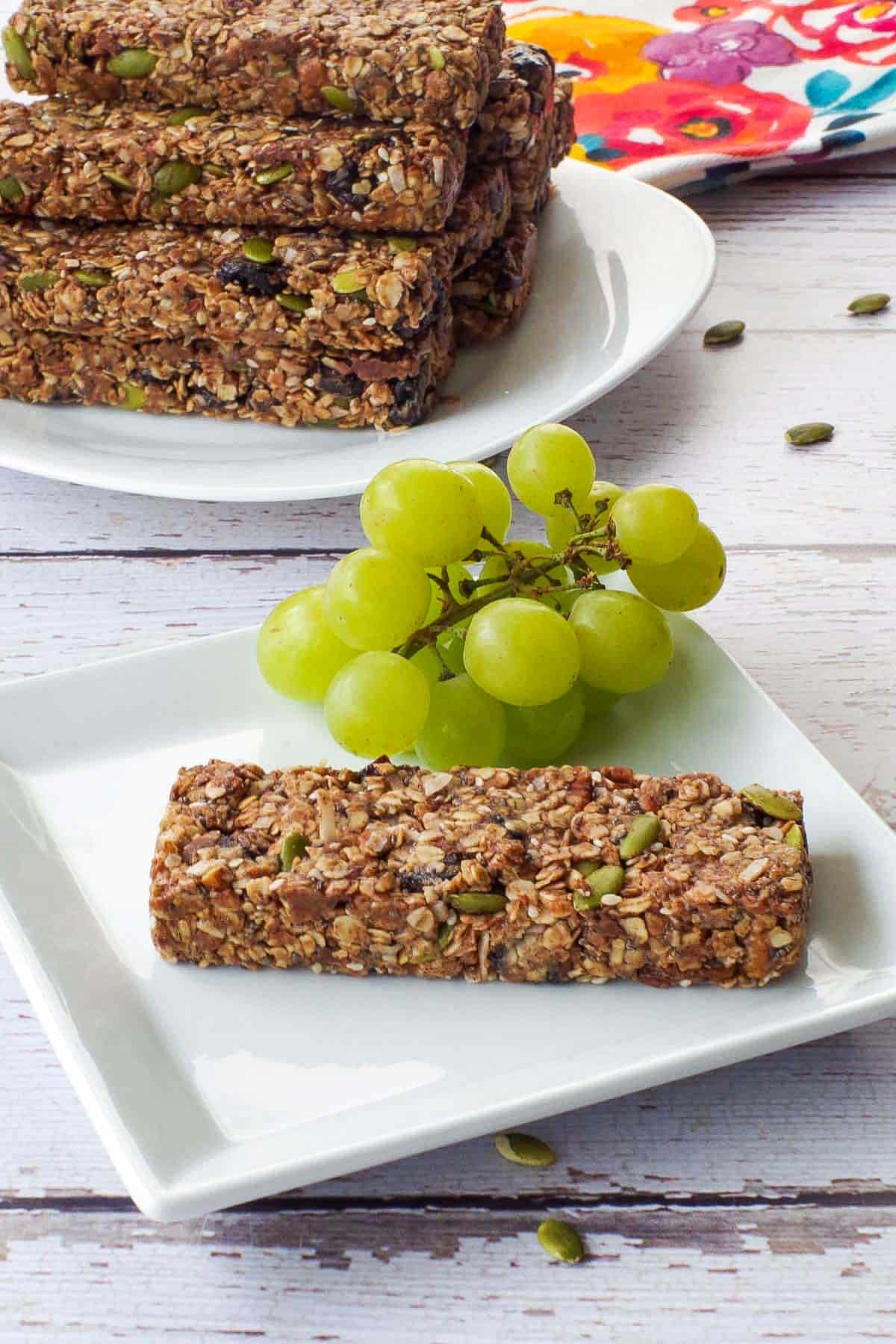 No Bake Almond Butter Granola Bar on a white plate with grapes and more granola bars on platter in the background.