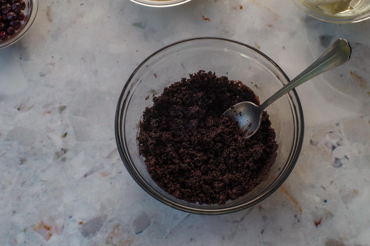 Baking crumbs and butter mixed together with a spoon in a medium glass bowl.