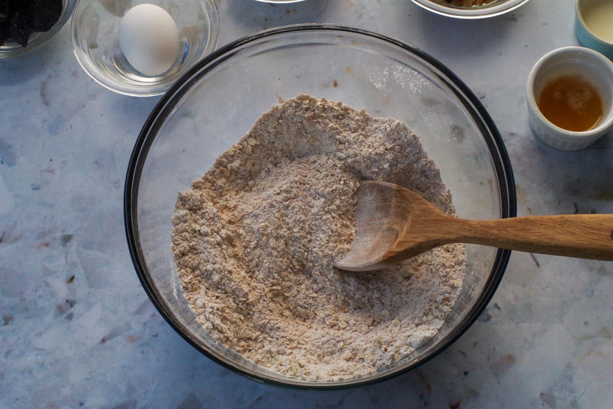 Dry ingredients in a large glass bowl with a wooden spoon.