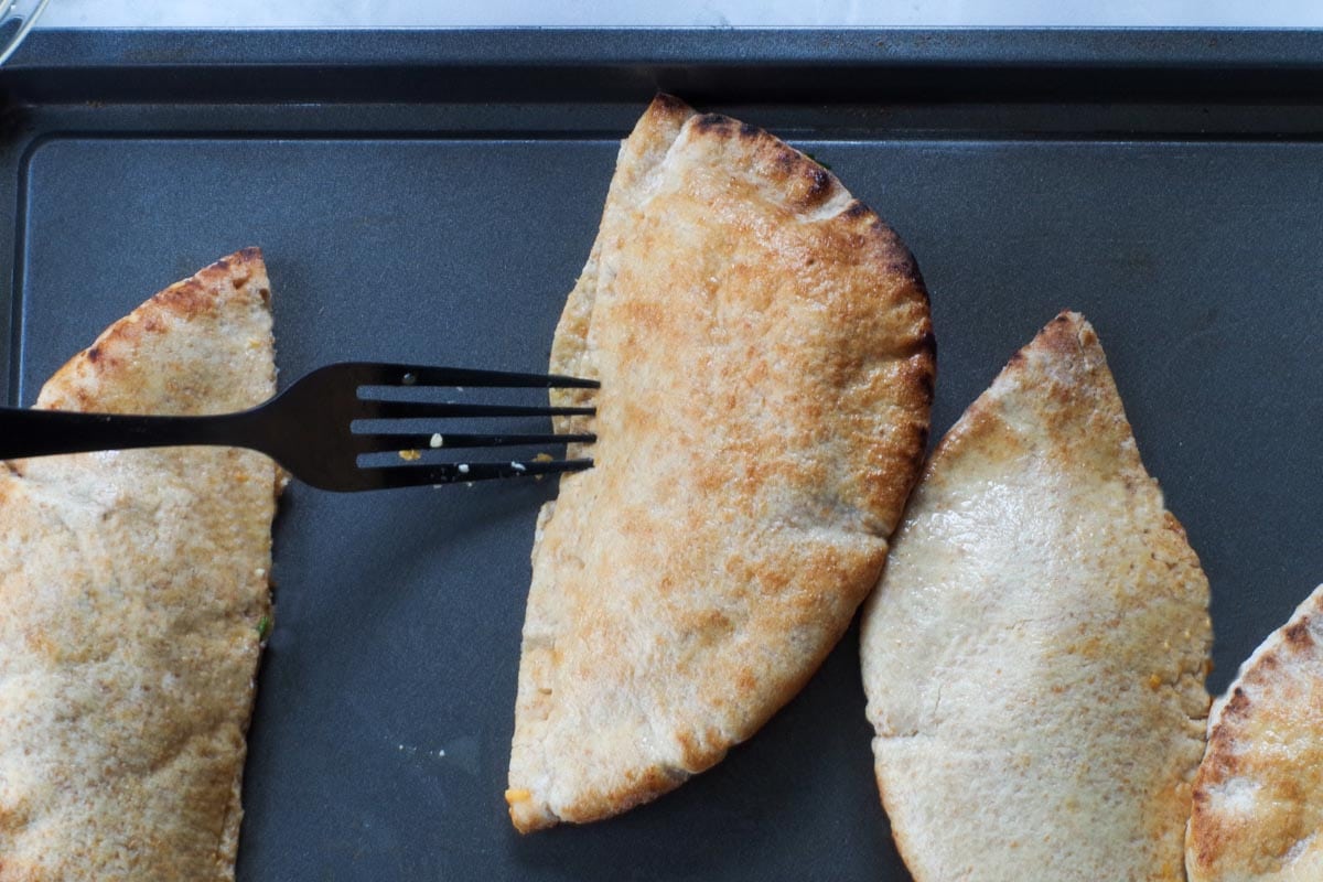 Pita being sealed with pork on baking sheet.