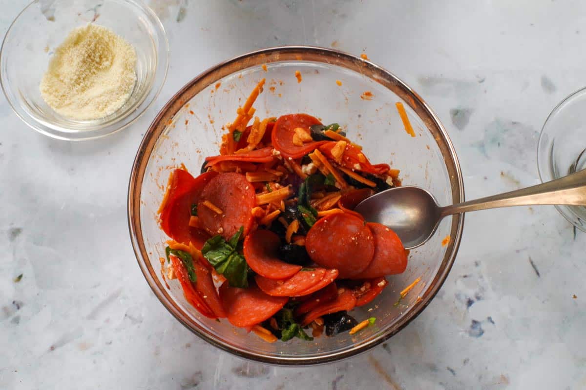Pizza pocket fillings in a glass bowl with a spoon.