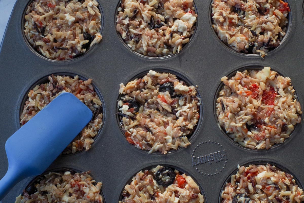 Rice cups being packed into muffin tins with blue spatula