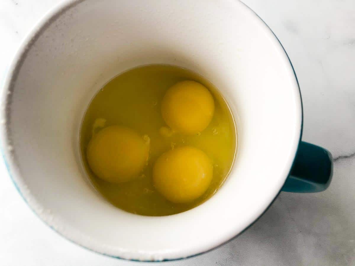 3 eggs cracked into a prepared microwave-safe mug.