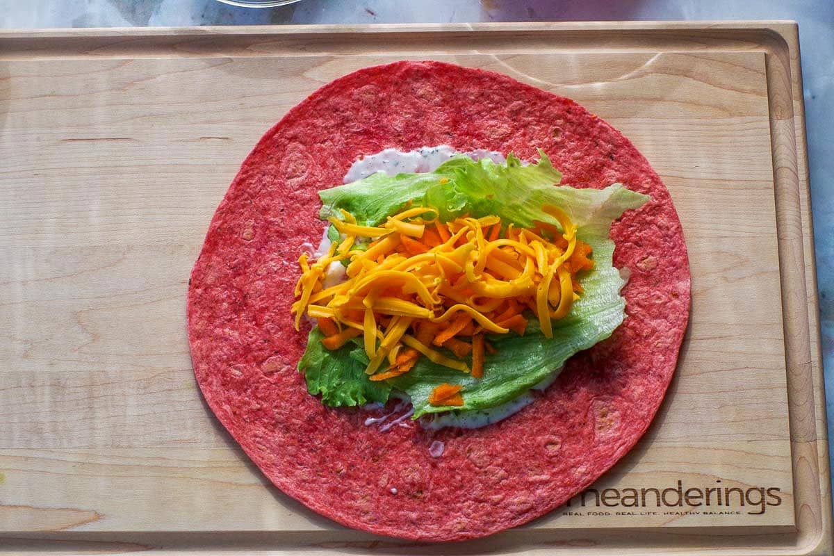 Tomato wrap with dressing, lettuce, cheese and shredded carrots in the middle.