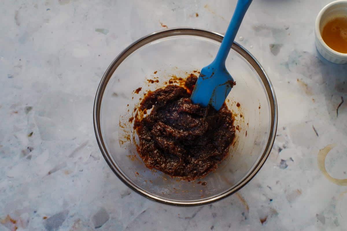 Prunes pureed with water in medium glass bowl with blue spatula.
