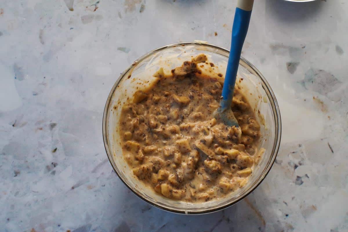 Prunes and coconut milk added to apple mixture in medium glass bowl with blue spatula.