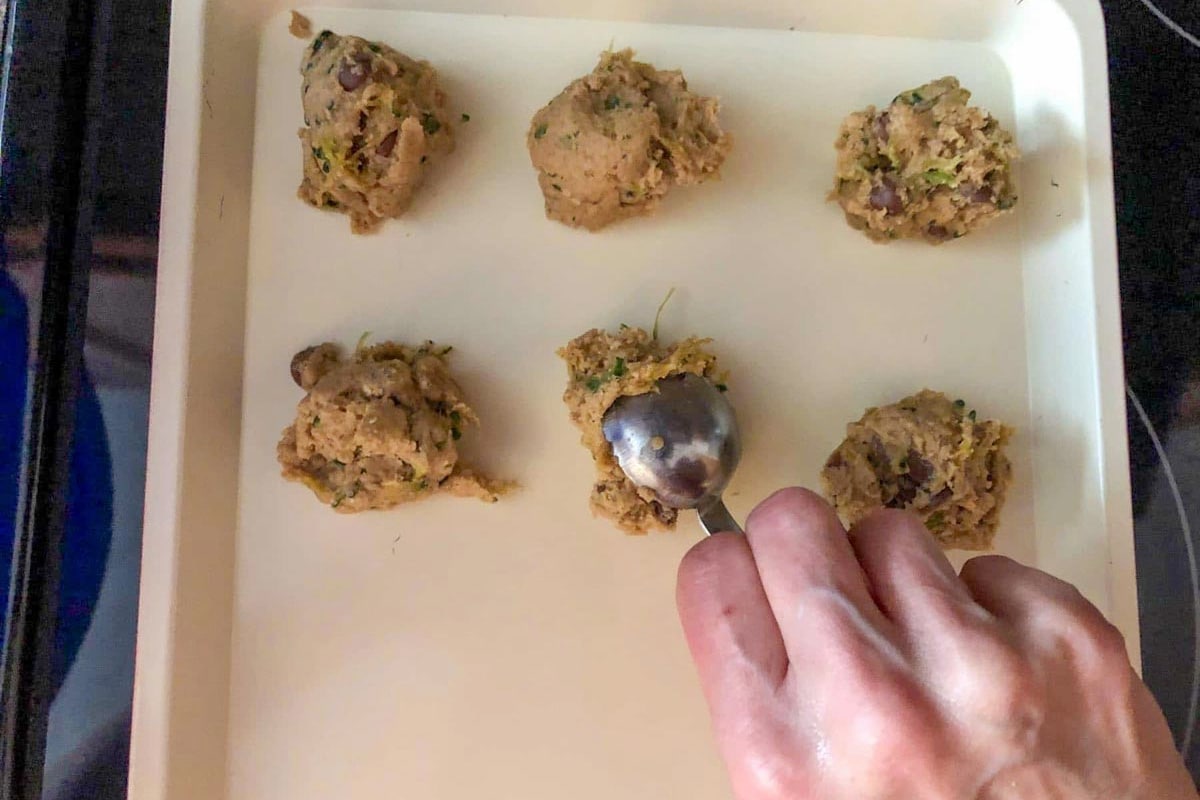 Raw cookie dough being dropped onto a cookie sheet.