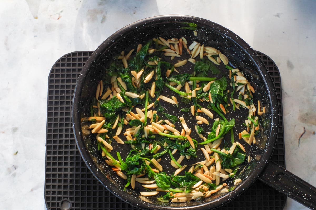Sage and spinach added to frying pan with nuts.
