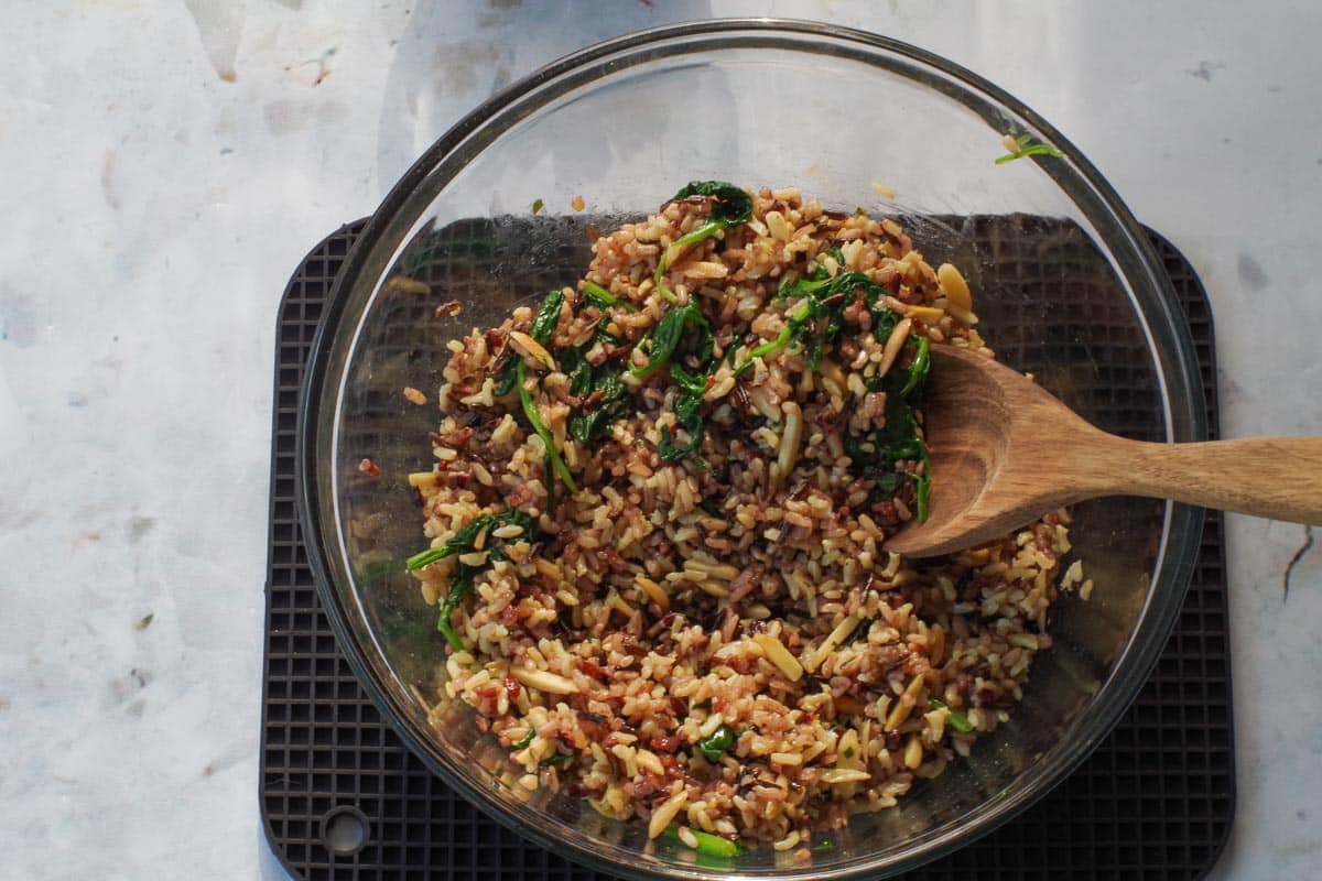 spinach and almonds stirred into rice mixture in glass bowl with wooden spoon
