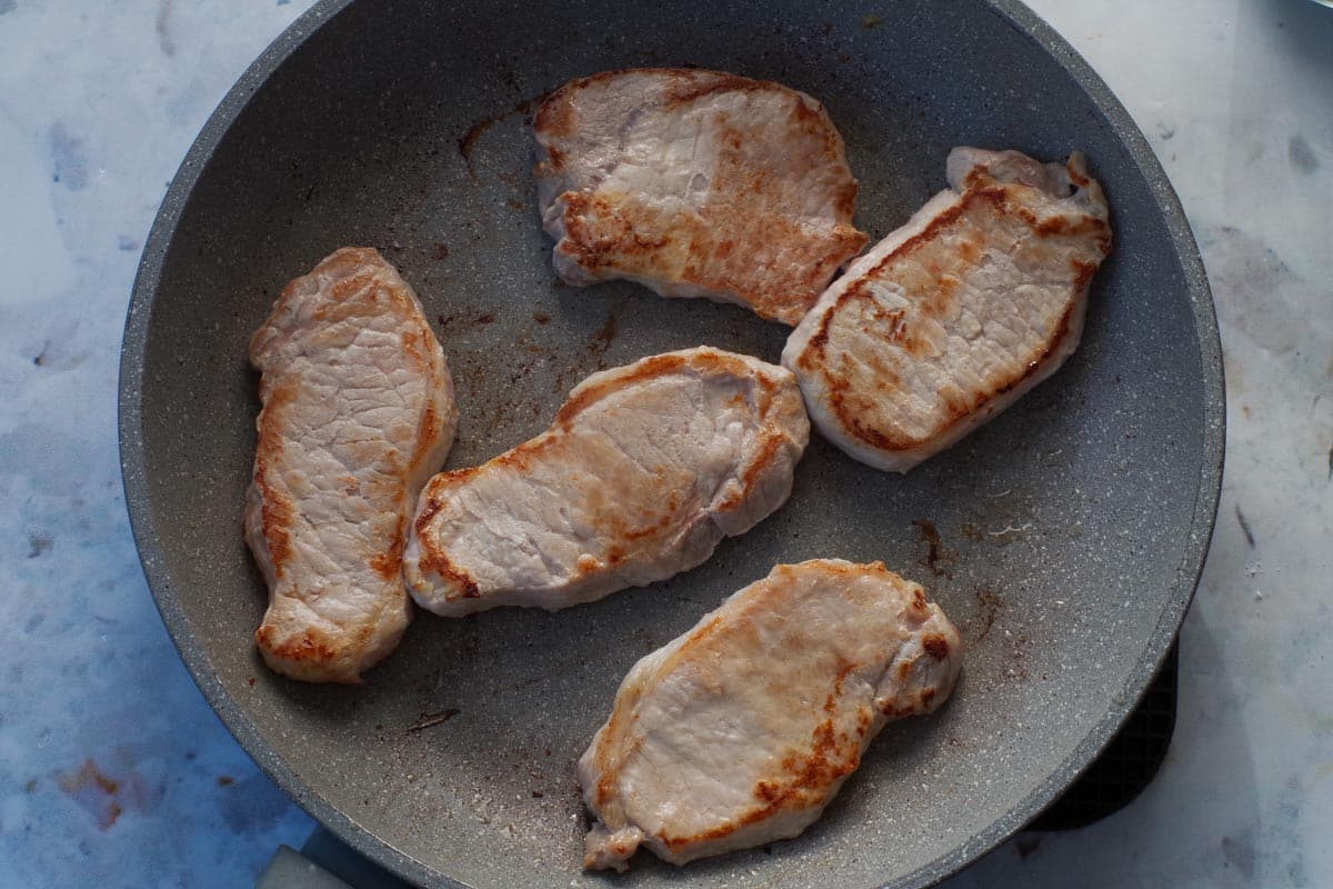 Pork cooking in frying pan.