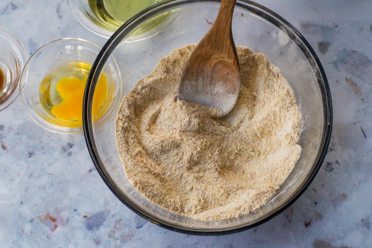 Dry ingredients mixed in large glass bowl with wooden spoon.