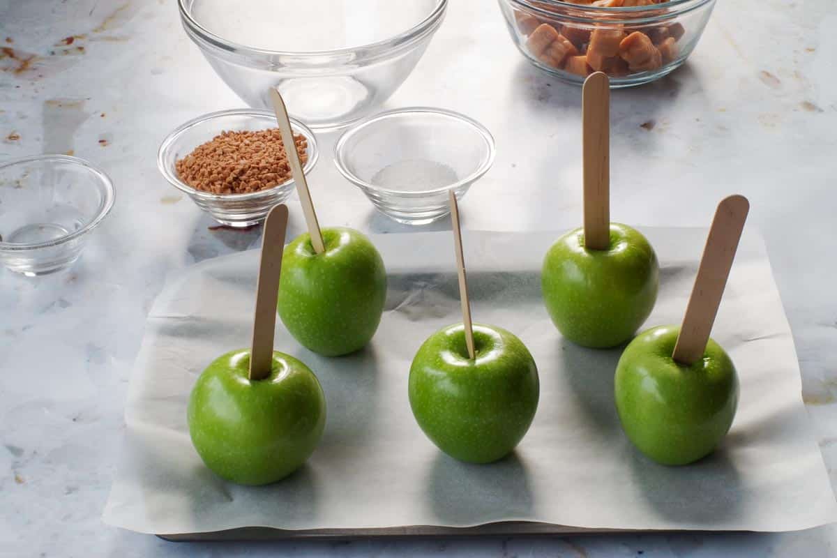 Apples on parchment covered baking sheet with popsicle sticks inserted in the top of each apple