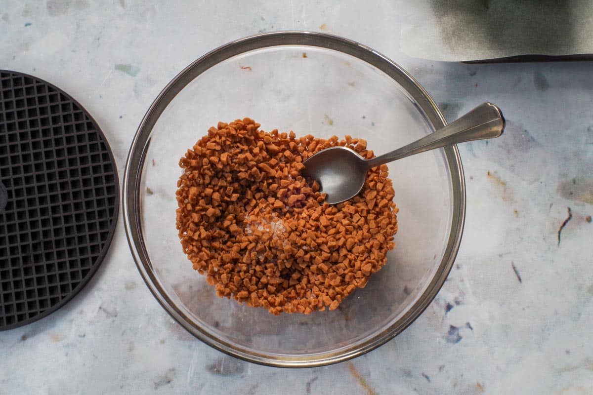 Toffee bits and salt mixed together in a glass bowl, with a spoon.