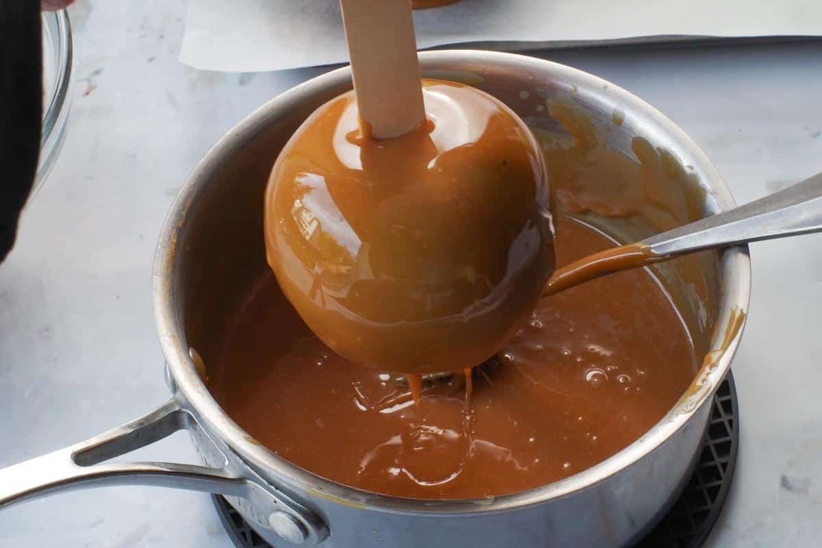 Caramel apple being swirled and lifted out of the pot.