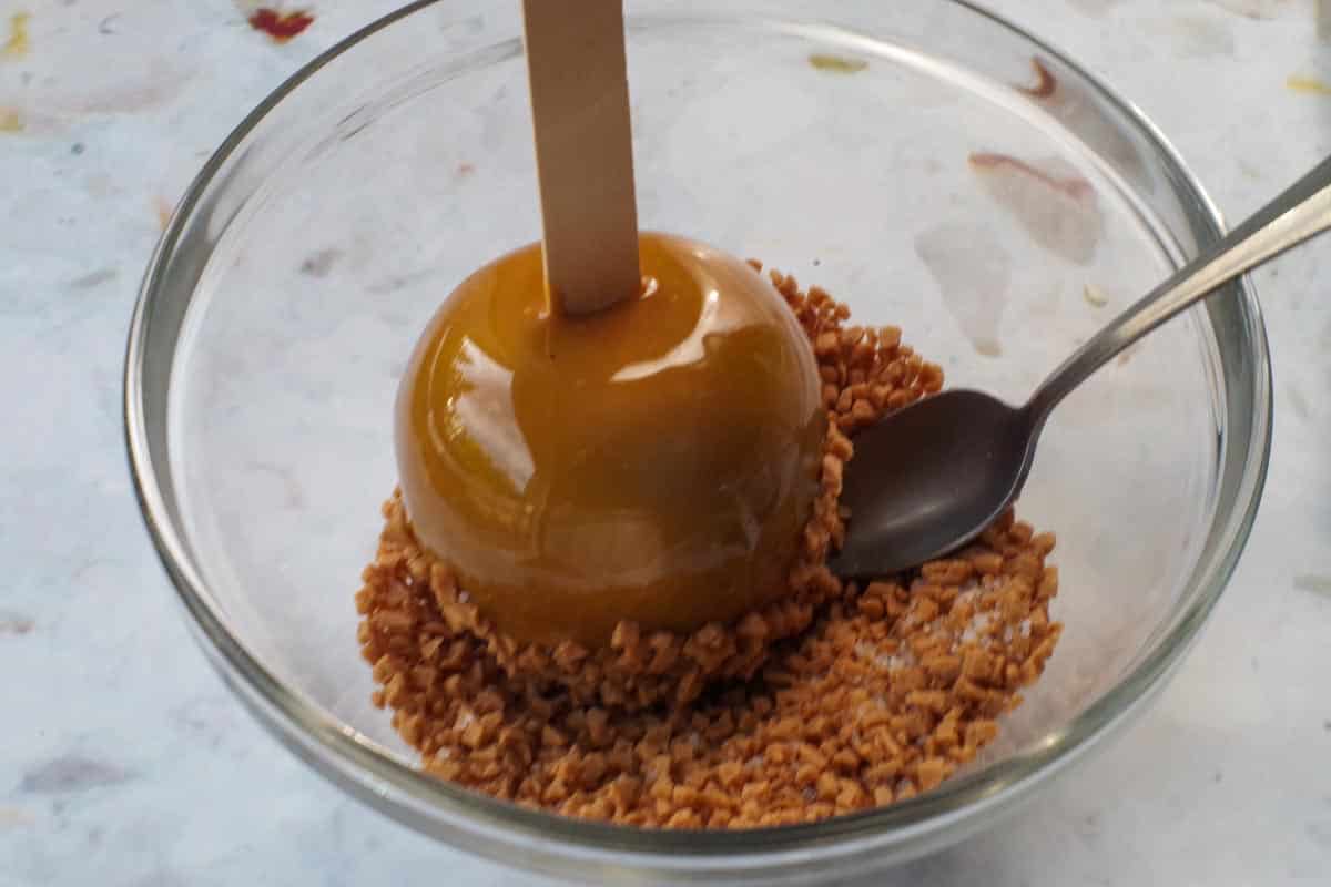 Caramel apple being dipped in salted toffee mixture.