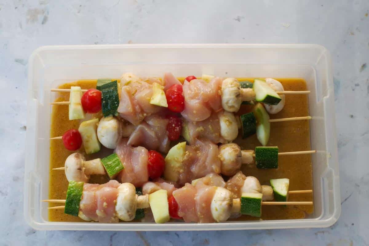 Kabobs in container with marinade poured over them.