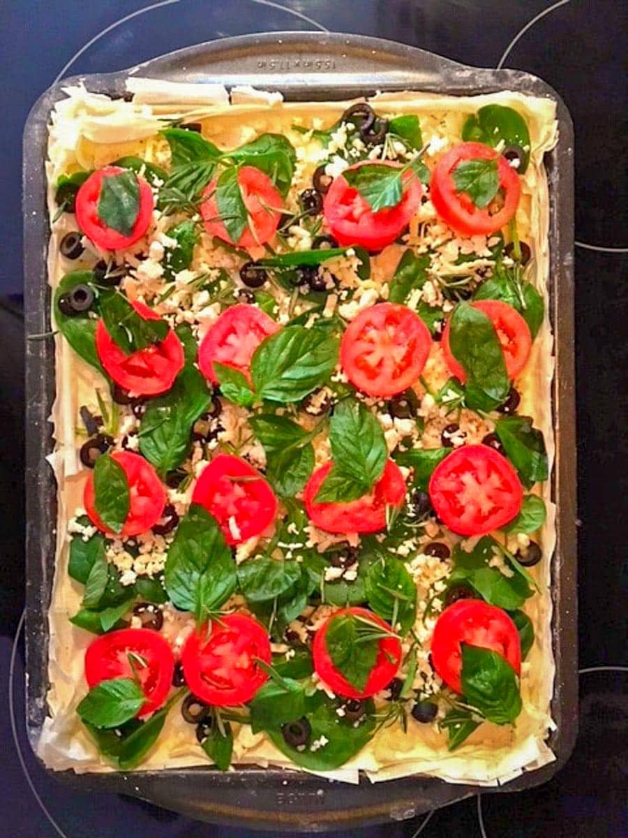 Spinach, black olives tomatoes and fresh herbs added to pizza.
