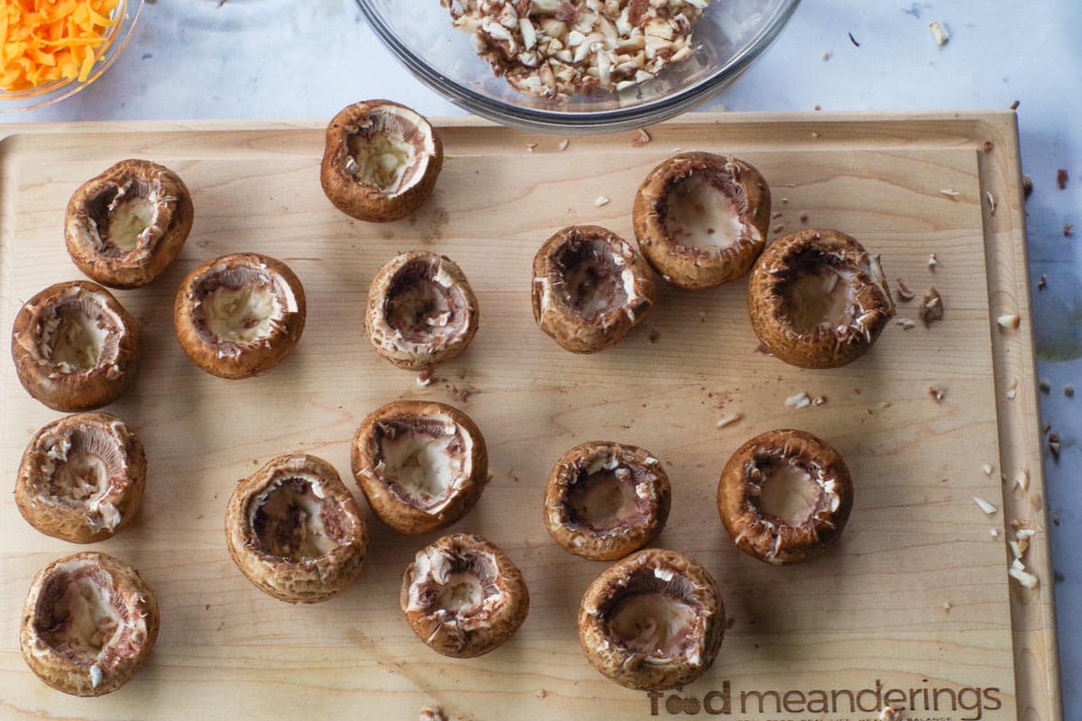 Mushrooms with insides scooped out, on a wooden cutting board.