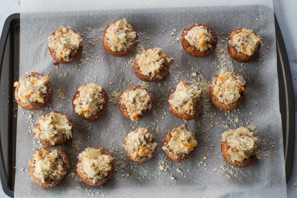 Potato stuffed mushroom caps sprinkled with parmesan cheese on parchment covered baking sheet.