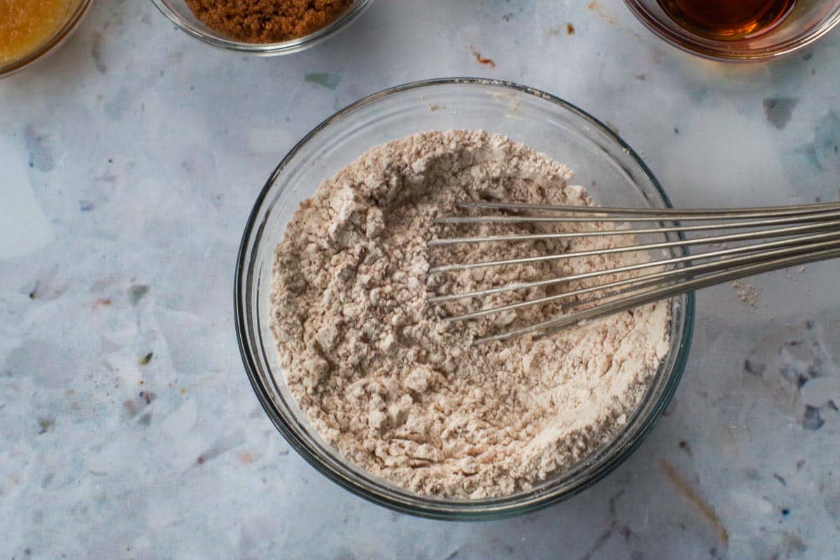 Dry ingredients in a glass bowl with a whisk.