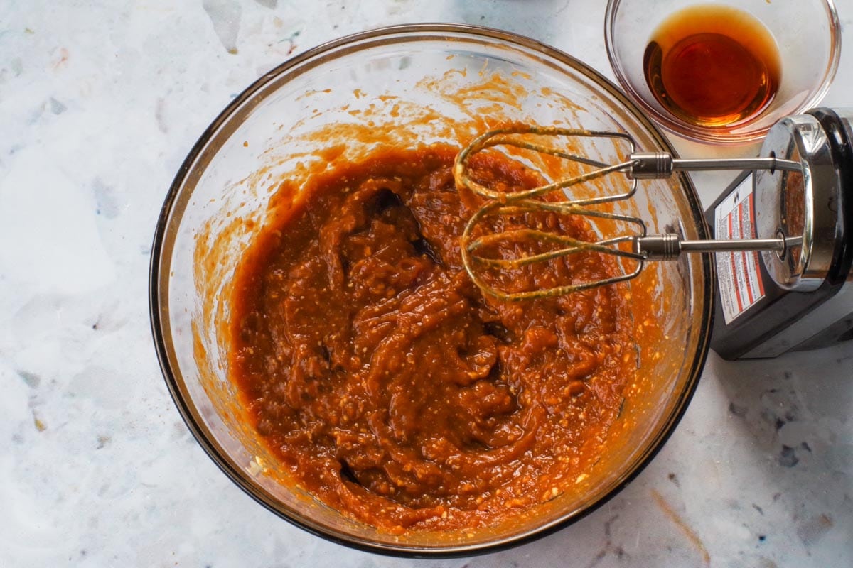 Butter, brown sugar, applesauce, pumpkin, and mashed banana beaten together in a glass bowl with beaters over bowl.