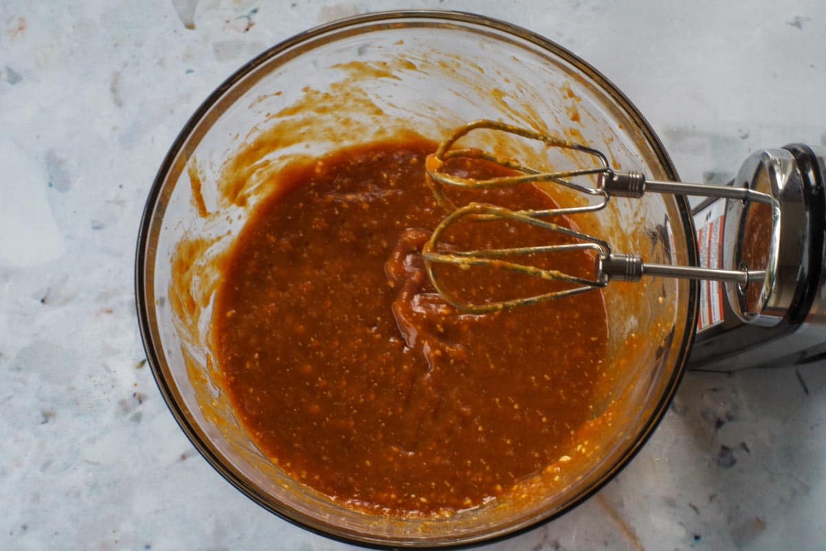 Egg whites, maple syrup and vanilla added to pumpkin mixture in glass bowl with beaters over bowl.