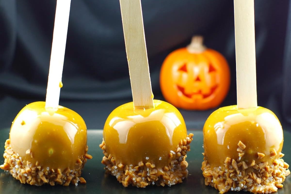 3 Salted Toffee Caramel Apples on a black try with a plastic jack o' lantern in the background.